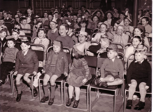Hall of seated children smartly dressed with party hats