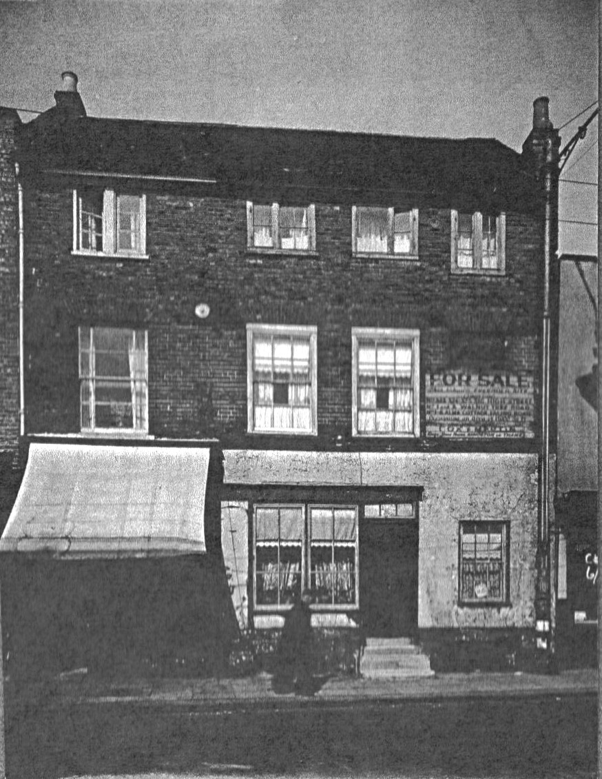 view showing a pair of 3 storey brick built properties; the ground floor of the left property is in shade from the shop canopy