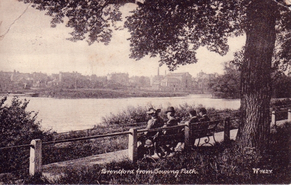 Sepia view taken from behind a seat occupied by a smartly dressed couple and their two sons, looking across the Thames towards Brentford, which appears hazily in the background