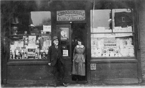 Couple standing in front of double-fronted shop 'T. Bradshaw 241 Family Millers'