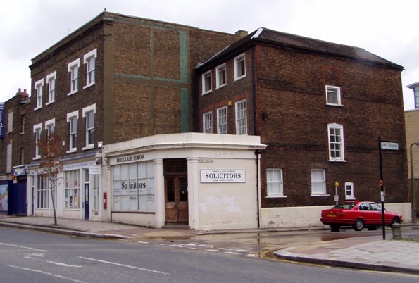 Corner brick built building with single storey extension to teh front and three storey buildings to rear and side on a wet day