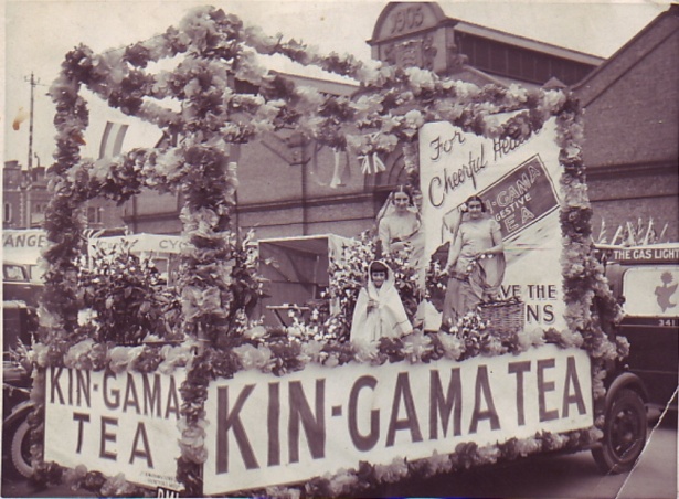 Garland-bestrewn float carrying two ladies and a small girl dressed as tea pickers in saris
